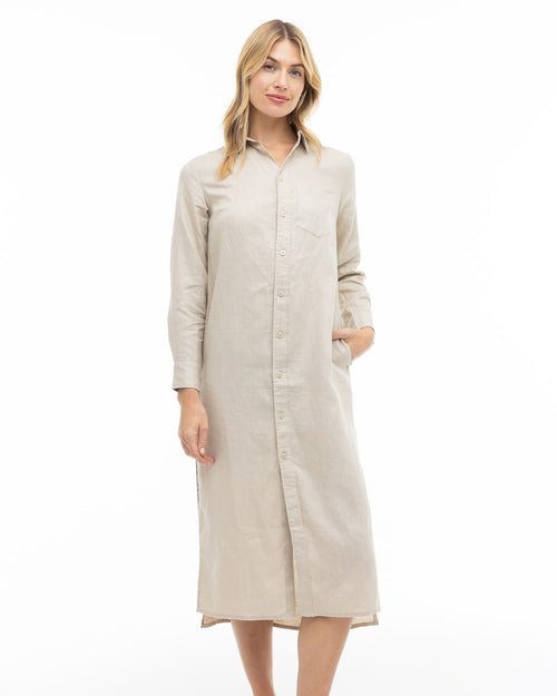 LIFESTYLE / EDITORIAL: Woman wearing a long sandstone-colored button-up dress with long sleeves, standing against white