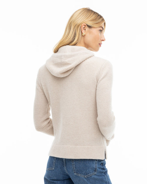 Side profile image of a woman wearing an oatmeal ribbed cashmere hoodie paired with blue jeans on white background