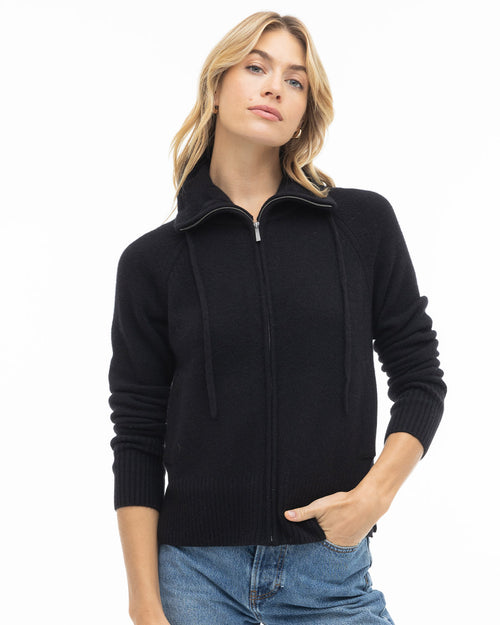 LIFESTYLE / EDITORIAL: Woman wearing black zip-up cashmere sweater with collar and drawstrings, paired with blue jeans