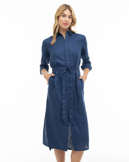 Woman wearing navy blue button-down midi dress with long sleeves and waist tie, standing against white background