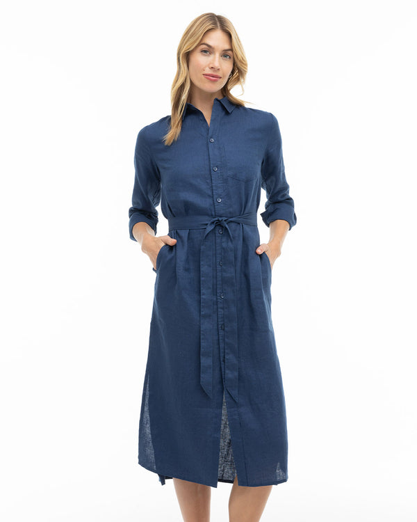Woman wearing navy blue button-down midi dress with long sleeves and waist tie, standing against white background