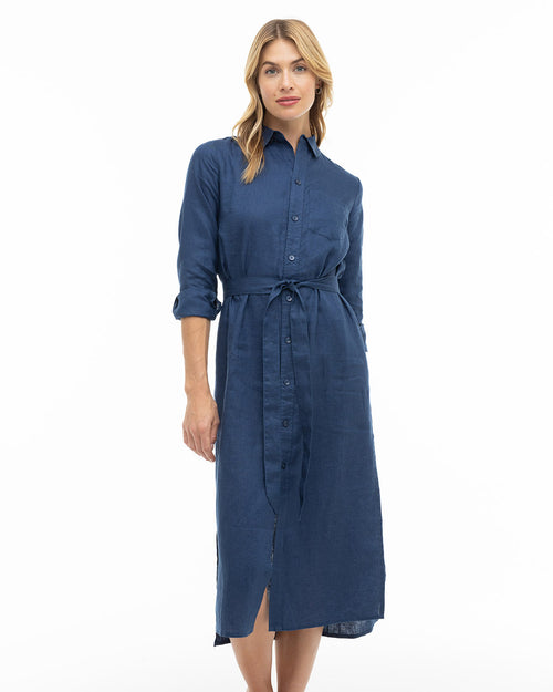 Woman wearing a navy blue long-sleeve button-down midi dress with a waist tie, standing against a white background