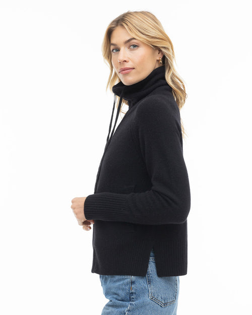 Woman wearing black cashmere turtleneck sweater with side slits and blue jeans, side profile on white background
