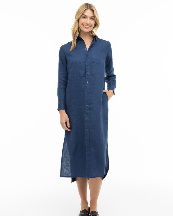 Woman wearing long navy button-down dress with collar and side pockets, standing against white background