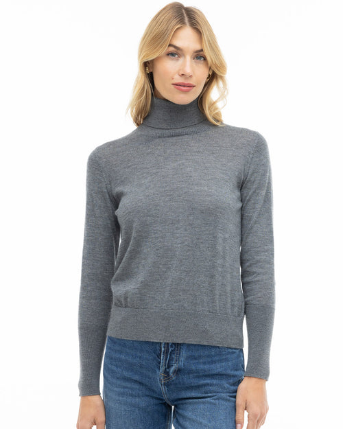 LIFESTYLE / EDITORIAL: Woman wearing a grey turtleneck cashmere sweater and blue jeans against a white background