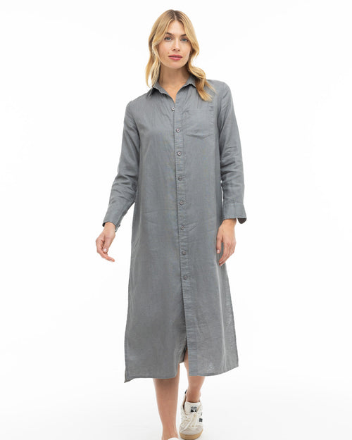 Woman wearing long graphite gray button-up dress with collar and sneakers, standing against white background