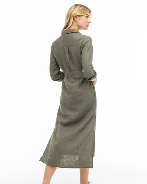 LIFESTYLE / EDITORIAL: Woman in dark olive long linen dress, back view, standing against white background