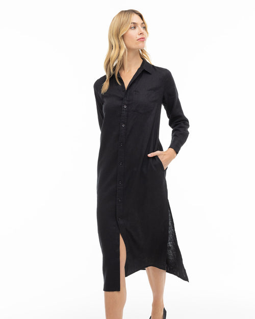 Woman wearing a black long-sleeve button-down midi dress with collar and side slit, standing against white background