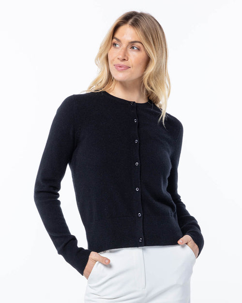 Woman wearing black buttoned cashmere cardigan with hands in pockets, looking to side against white background