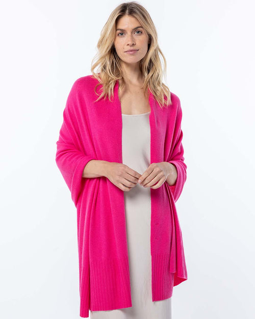 Front view image of a woman wearing a bright pink luxury cashmere wrap over a light beige dress against white background