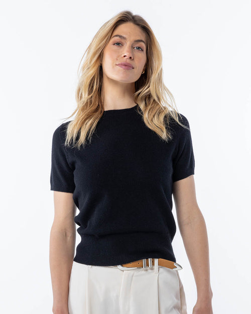 LIFESTYLE / EDITORIAL: Woman wearing black short-sleeve cashmere sweater and white pants against white background