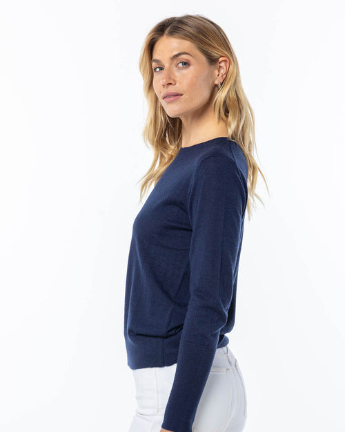LIFESTYLE / EDITORIAL: Woman wearing navy blue cashmere sweater and white pants, posing sideways against white background