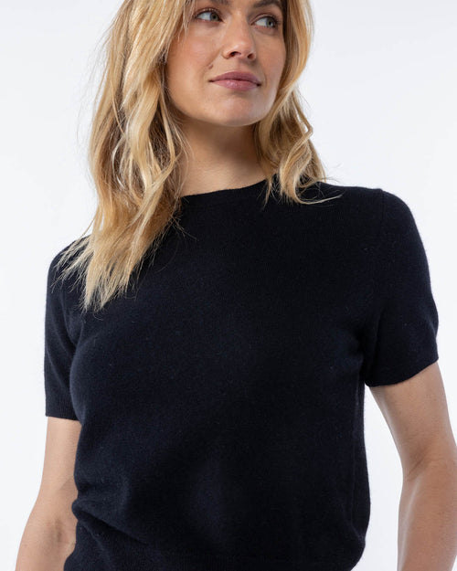 Woman wearing short-sleeve black cashmere sweater, shown from chest up against white background