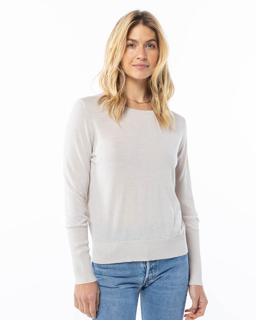 Front-facing image of a woman wearing an oatmeal cashmere sweater with light blue jeans on white background