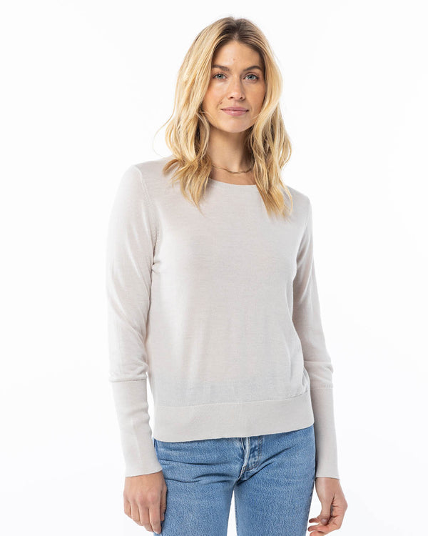 Front-facing image of a woman wearing an oatmeal cashmere sweater with light blue jeans on white background