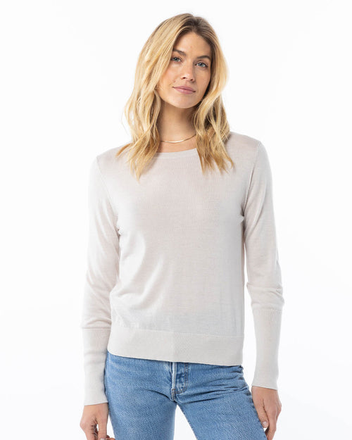 Front view image of a woman wearing an oatmeal cashmere sweater paired with blue jeans against white background