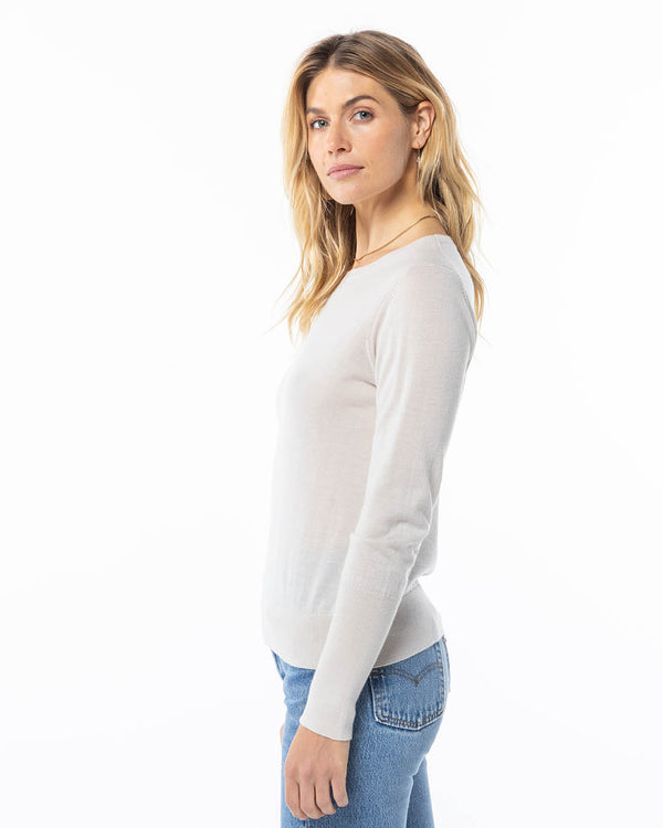 LIFESTYLE / EDITORIAL: Woman in oatmeal cashmere sweater and blue jeans, standing sideways against white background