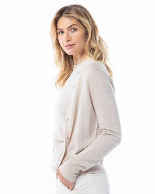 Three-quarter view image of a woman wearing an oatmeal cashmere cardigan, standing with a slight smile on a white background