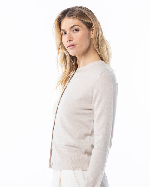LIFESTYLE / EDITORIAL: Woman wearing oatmeal-colored cashmere cardigan, side view, neutral background