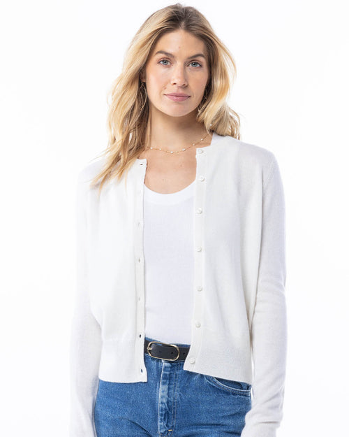 Front-facing image of a woman wearing a white cashmere cardigan paired with a white tank top and blue jeans