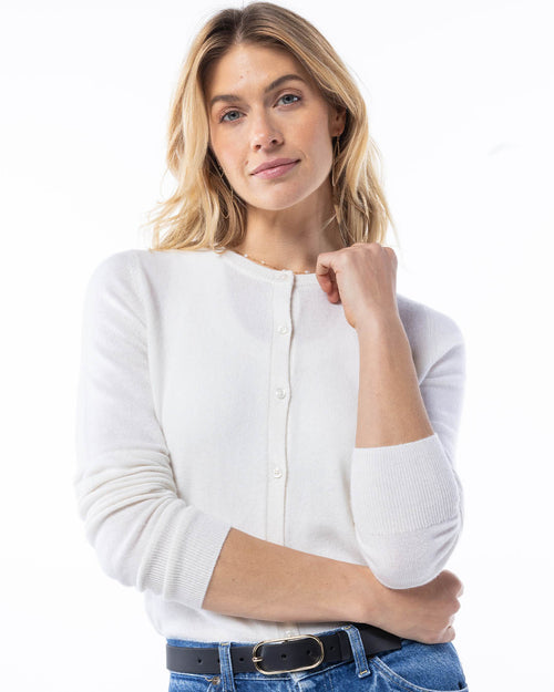 LIFESTYLE / EDITORIAL: Woman wearing white cashmere cardigan with pearl buttons and blue jeans against white background