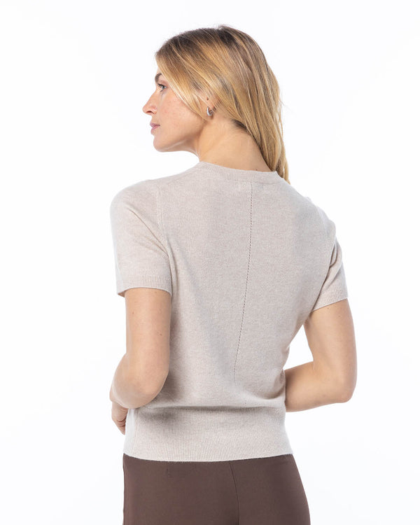 Woman wearing oatmeal-colored short-sleeve cashmere sweater, back view, standing against white background