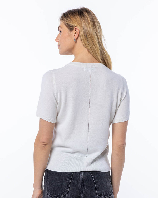 LIFESTYLE / EDITORIAL: Woman wearing white short-sleeve cashmere sweater, back view, paired with black jeans against white
