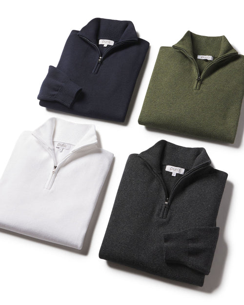 LIFESTYLE / EDITORIAL: Four folded quarter-zip cashmere sweaters in navy, olive, white, and charcoal on white background