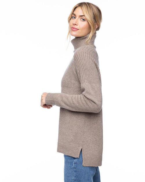 Side view of woman wearing vintage khaki half-rib turtleneck cashmere sweater with side slit and blue jeans against white