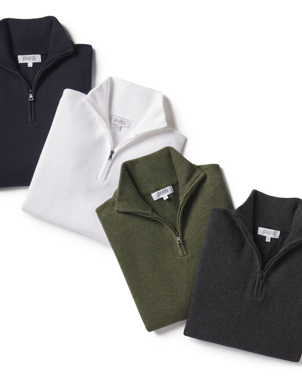 Four folded quarter-zip cashmere sweaters in black, white, olive green, and dark gray on white background