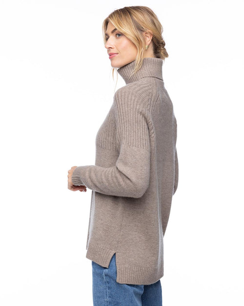 Woman in vintage khaki half-rib turtleneck cashmere sweater, side view, paired with blue jeans on white background