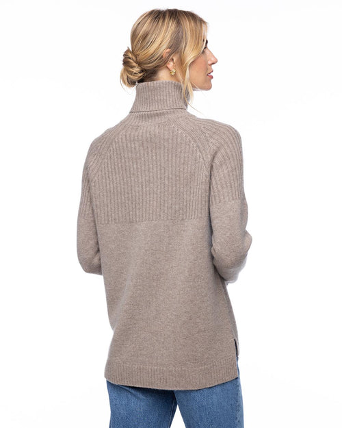 Woman wearing vintage khaki half-rib turtleneck cashmere sweater, back view, paired with blue jeans against white background