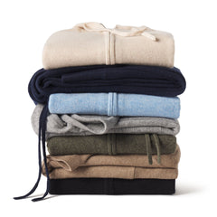 Stack of folded cashmere sweaters in beige, navy, light blue, gray, olive, brown, and black colors on white background