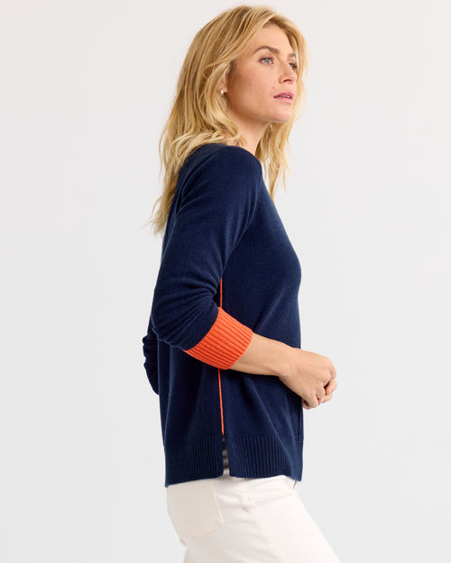 LIFESTYLE / EDITORIAL: Woman wearing navy and orange cashmere sweater, standing sideways against a plain background
