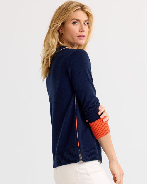 LIFESTYLE / EDITORIAL: Woman wearing navy and orange cashmere sweater, looking over shoulder against white background