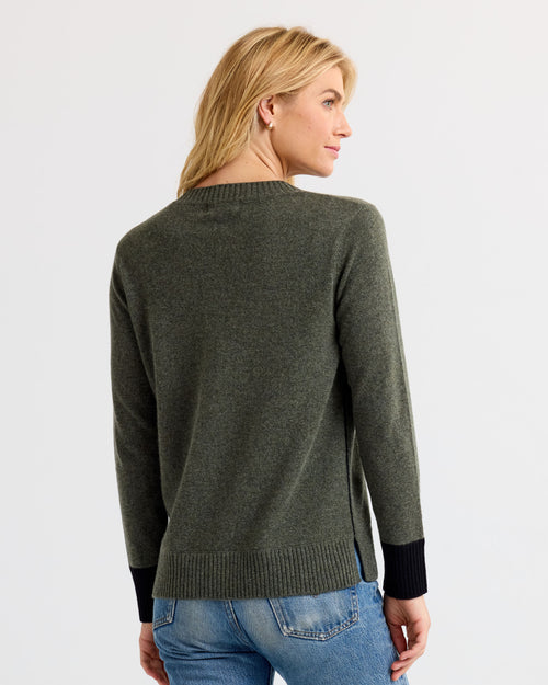 Woman wearing dark olive cashmere sweater with black cuffs, viewed from the back, paired with blue jeans