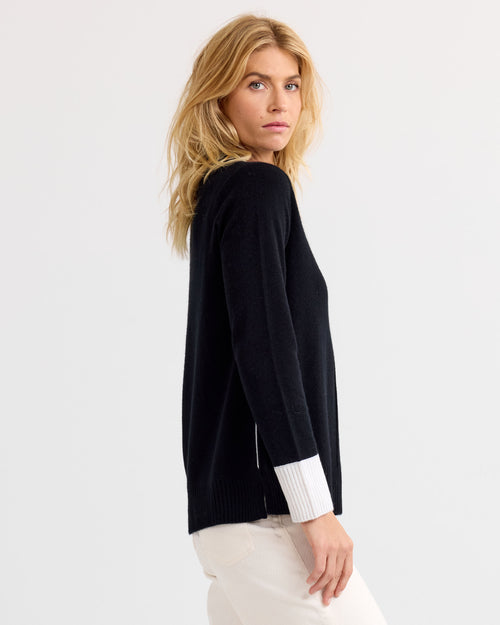 Woman in black cashmere sweater with white cuffs, side view, against plain light background