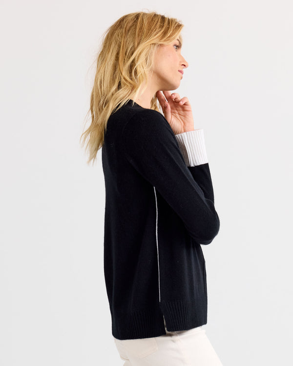 LIFESTYLE / EDITORIAL: Side view of woman wearing black and white cashmere sweater against plain background