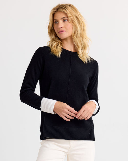 Three-quarter view image of a woman wearing a black cashmere sweater with white cuffs and white pants
