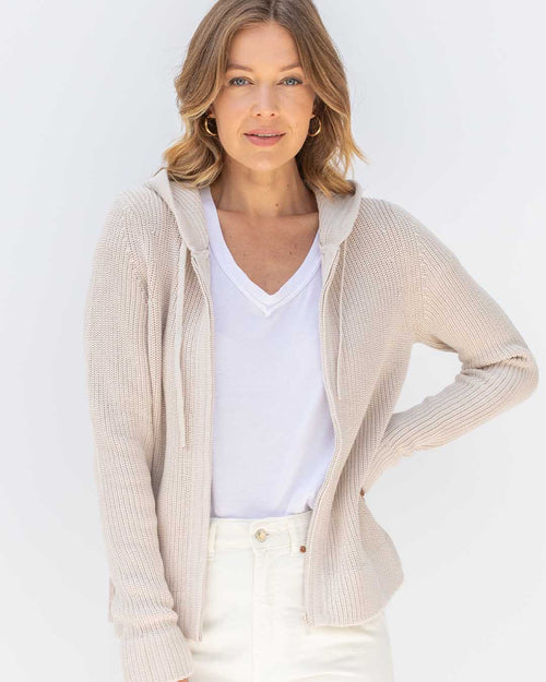 LIFESTYLE / EDITORIAL: Woman wearing oatmeal-colored cotton hoodie over white V-neck shirt and white pants against white