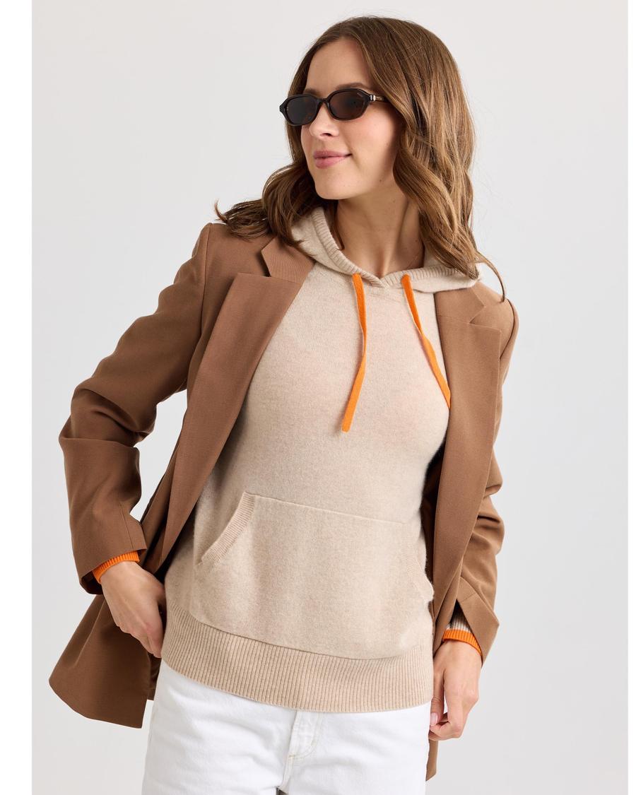 Sand cashmere hoodie with orange drawstring and orange-edged cuffs, worn open under a blazer.