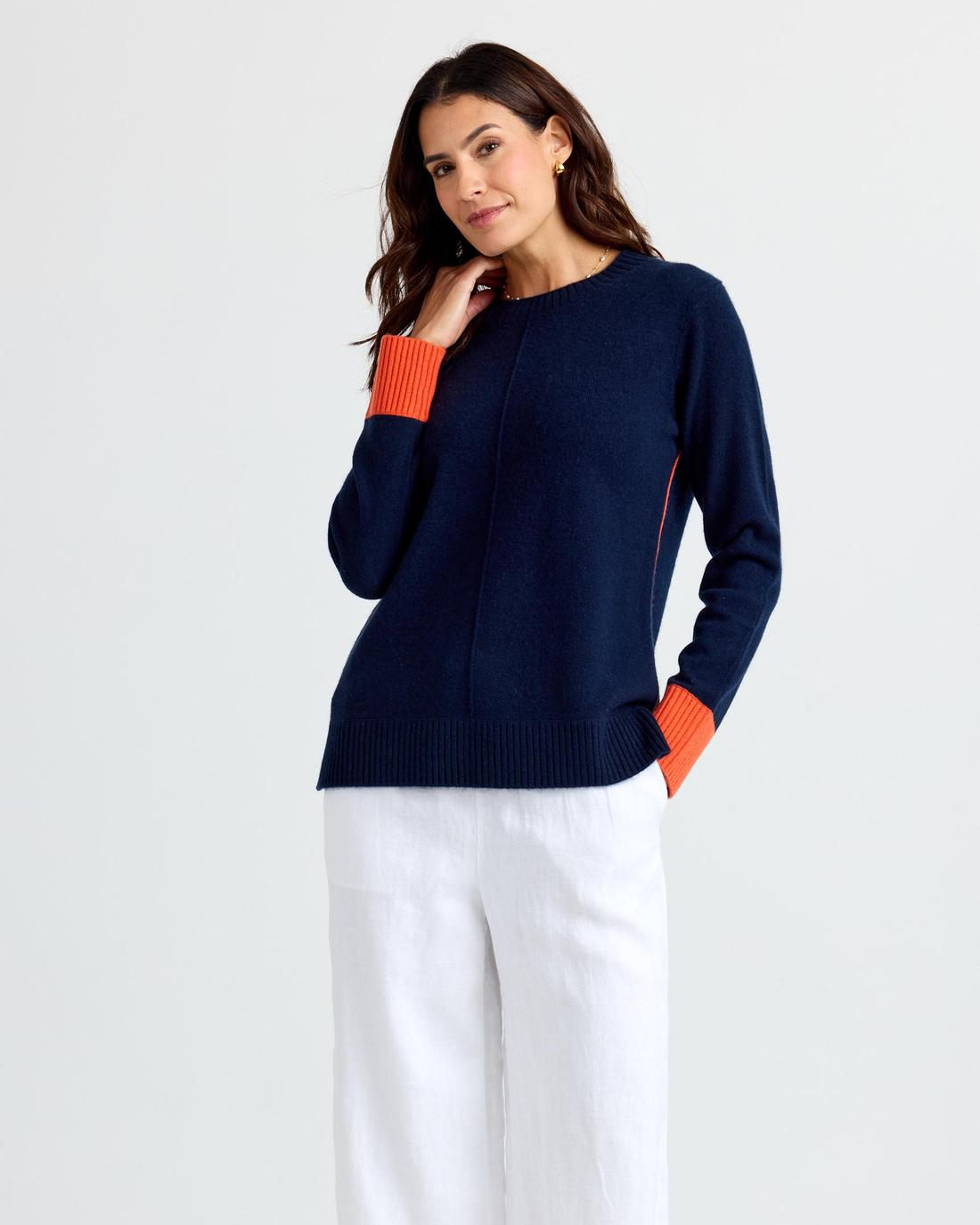 Navy cashmere crew with orange turnback cuffs and a fine orange piping line, worn on the model.